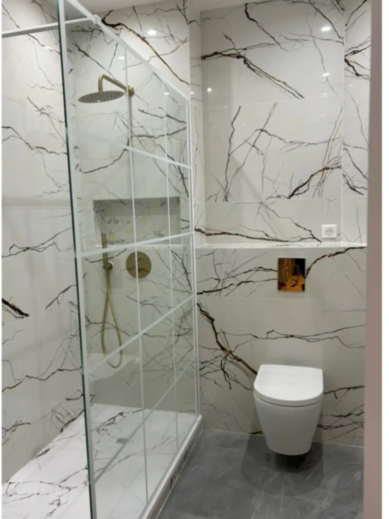 Salle de bain après rénovation : faïence effet marbre blanc veiné, douche à l'italienne et robinetterie dorée.